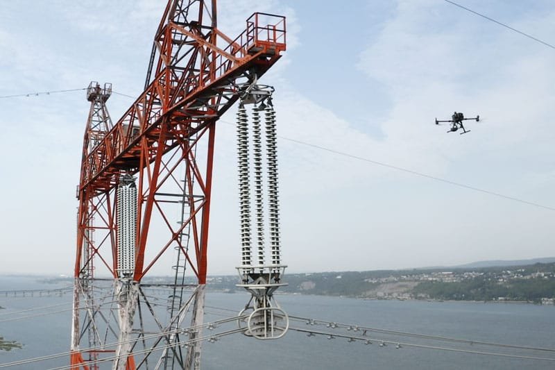 Un drone survole un pylône électrique de haute tension, capturant des images détaillées pour l'inspection des infrastructures.